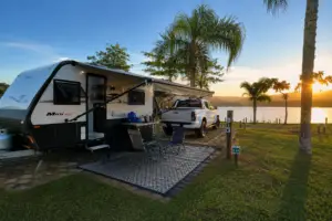 Trailer em camping brasileiro durante viagem de caravanismo, estacionado à beira de lago com estrutura de camping e área externa montada.
