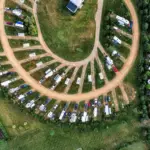 Vista aérea de camping para RVs com motorhomes e trailers estacionados em vagas gramadas ao redor de ruas de terra.