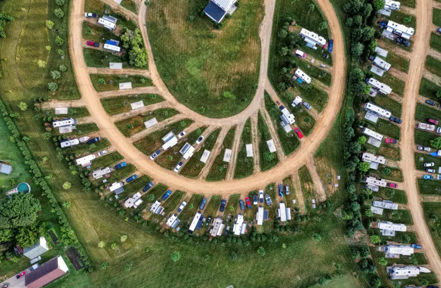 Vista aérea de camping para RVs com motorhomes e trailers estacionados em vagas gramadas ao redor de ruas de terra.