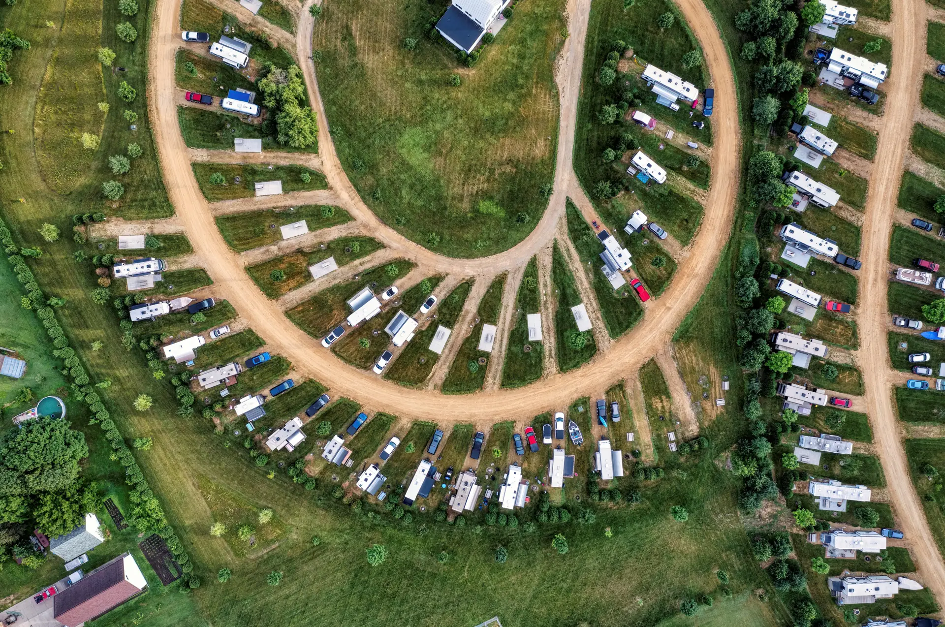 Vista aérea de camping para RVs com motorhomes e trailers estacionados em vagas gramadas ao redor de ruas de terra.
